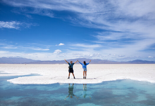 Young man and woman in love posing in the Salinas Grandes of Argentina during their vacation at the edge of a blue lake in which they are reflected.