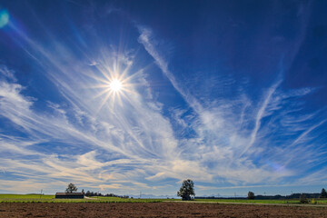 Blue sky with light clouds and a pattern of exhaust vapor trails from aircraft