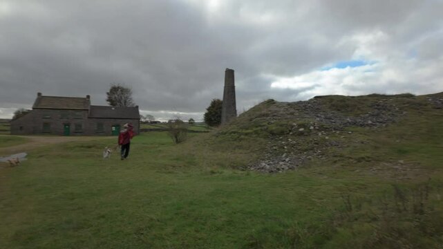SHELDON, DERBYSHIRE, ENGLAND - OCTOBER 17 2024: Woman wearing a red jacket walking her dogs at Magpie Mine in the Peak District National Park.