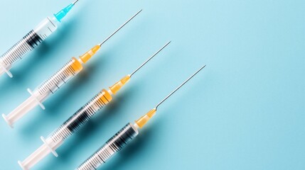 Four syringes with colored liquid and needles arranged on a light blue background, symbolizing vaccination or medical treatment.