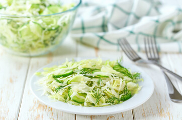 healthy vegetable salad of cabbage, cucumber and dill on a wooden table, selective focus.