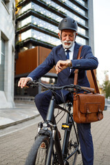 Senior commuter with helmet and bag checking time while traveling to work on bicycle in modern city