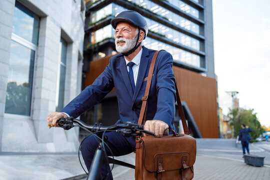 Confident senior entrepreneur in cycling helmet riding bicycle and commuting to work in modern city