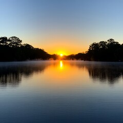 Fototapeta premium A tranquil sunrise over a misty lake, with the sun reflecting off the water.