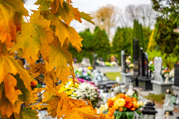 Graves with candles during the All Souls' Day celebration on November 1st. Golden, autumn leaves in the foreground. Photo taken during the day in natural light
