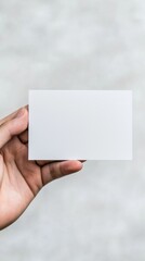 Obraz premium Hand holding a blank card against a soft grey background, perfect for customization or branding purposes.