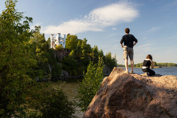 Monrepos Park, Vyborg, Leningrad Region, Russia. A young man and a woman are sightseeing. The Ludwigsburg Chapel is visible in the distance on the rocky island of Ludwigstein. Beautiful landscape.