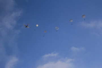 Paratroopers descend from a military aircraft on a clear day against a blue sky, showcasing airborne training and teamwork