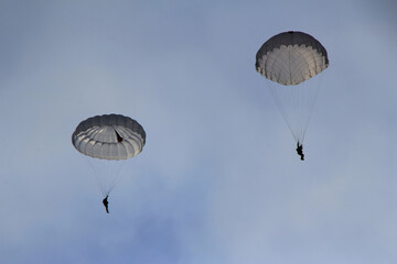 Two skydivers glide through the air, suspended beneath their parachutes, showcasing an adventurous...