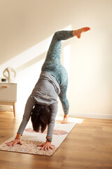 Young woman practicing yoga at home, standing in Vrksasana exercise