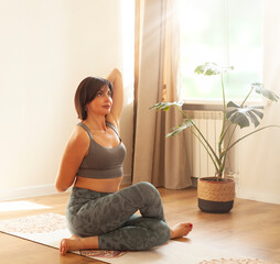 Young woman practicing yoga at home, sitting on the floor in lotus position