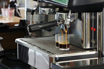Freshly brewed espresso pours from a professional coffee machine into a glass cup on counter bar in cafe