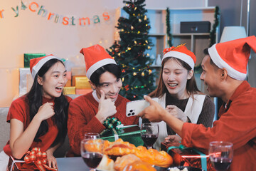 Group of young Asian man and women as friends having fun at a New Year's celebration, holding gift boxes standing by Christmas tree decoration, midnight countdown Party at home with holiday season.
