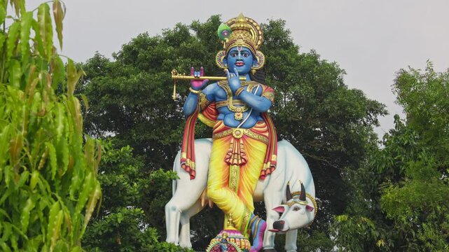 Closeup of big Lord Krishna with holy cow statue on the temple with big tree in background