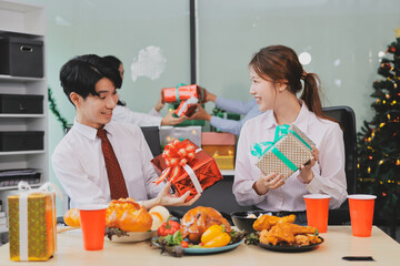 full length view of a group of business team wearing red Santa hat and exchange gift box together in the office for Christmas.