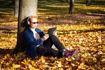 Asian man looking to the digital tablet screen while sitting in nature Autumn park