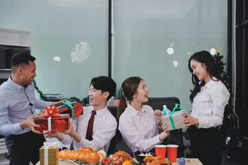 full length view of a group of business team wearing red Santa hat and exchange gift box together in the office for Christmas.