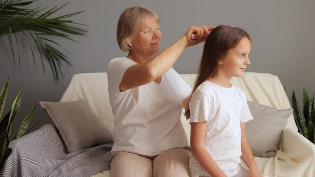 Loving grandmother gently combing brushing her little granddaughter's hair enjoying family time together bonding at home with care sharing calm bonding at home