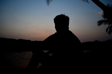 Silhouette of a person sitting on the rocks fronting sunset, display a moment of breeze and calm.