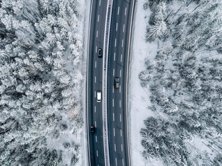 Aerial drone view of winter landscape road with cars and truck driving. Highway with cars in winter season and snow covered trees.