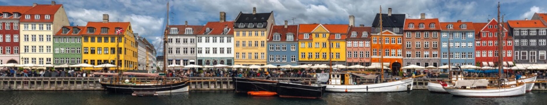 Ultra wide summer cityscape panorama of Nyhavn (New Harbour) in Copenhagen, Denmark. Panoramic view of iconic waterfront featuring colorful 17th-century danish houses, sailing ships and caf&eacute;s