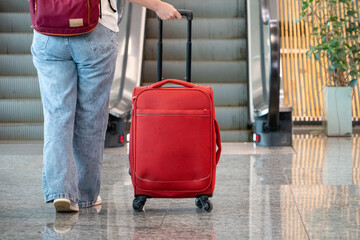 Mujer viajera caminando por aeropuerto con su maleta roja