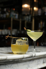 Two cocktails in classic martini and whiskey glass with feijoa on a bar counter, close-up