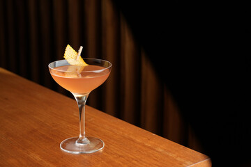 Bronx cocktail glass with orange peel slice on a wooden bar counter, background with copy space
