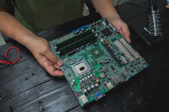 Asian male computer repairman is checking and fixing hardware problems on computers and replacing broken parts and improving performance.