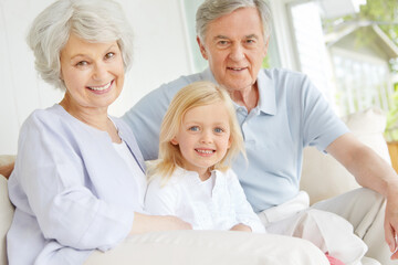 Obraz premium Grandparents, portrait and happy in home with grandchild for bonding, care and weekend visit on sofa. Elderly people, face and family in living room with little girl for relax, support and connection