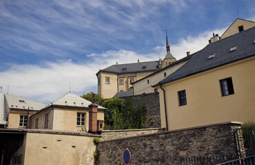 A castle on top of a hill. Houses under the hill. Castle complex. Castle with houses in the castle grounds. Blue sky with white clouds. Summer, travel, monuments, tourism.