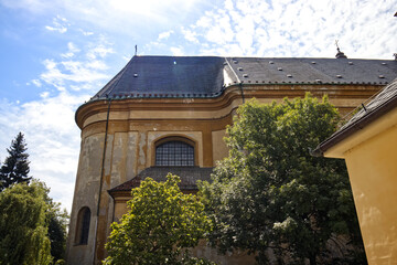 Monastery building. Brick wall in front of the building of the old monastery. Trees and a monastery garden. Sun rays shining through the clouds in the sky. Monastery, old historical building.