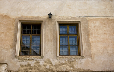 Two rectangular windows with bars. Windows of an old castle building. Decorative lamp on the wall above the windows. Old decaying facade. Windows, glass, lamp, fallen facade, rough, broken