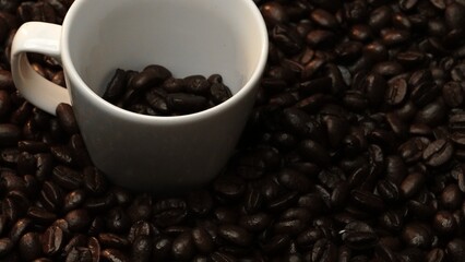 Close up of coffee bean falling in to coffee cup surrounded by pile of beans. Dropping aromatic blending bean in to white cup. Top view of coffee drop in to glass with black background. Comestible.