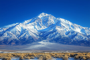 Snow-capped mountains rise majestically under a vivid blue sky, showcasing nature's grandeur and serenity in a winter landscape