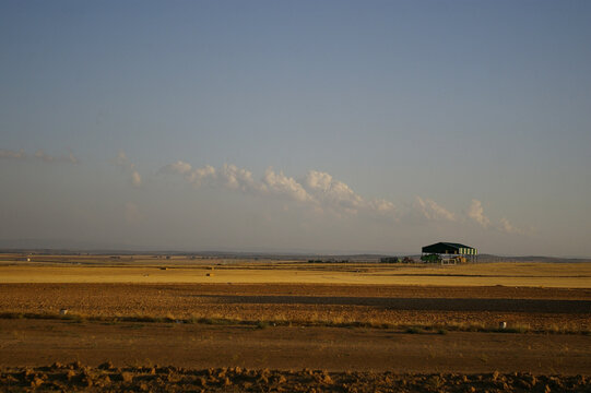 Paisaje de campos de sembrado con nubes al atardecer, agricultura de secano, un aparcamiento para tractores y maquinaria agr&iacute;cola y guardar fajos de paja
