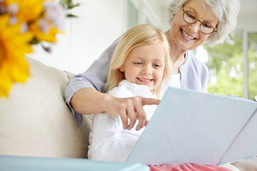 House, grandmother and girl on couch, reading book and bonding together in living room. Apartment, senior woman and granddaughter on sofa, education and smile with fantasy, support and care in lounge