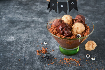 Halloween party chocolate puddings or Panna Cotta with brownie crumbles and chocolate sculls served in clear glass on grey dark background. Party idea for Halloween.