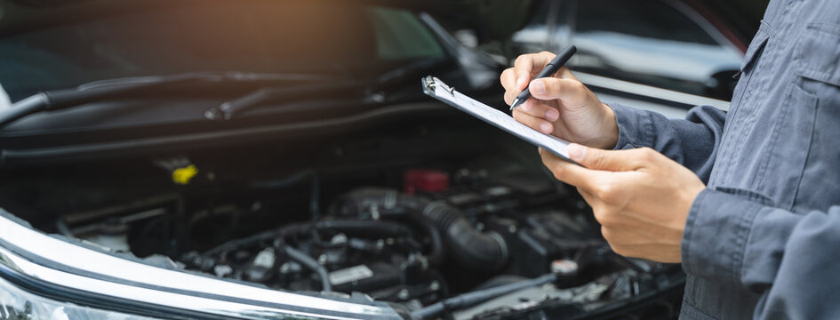 Auto check up and car service shop concept. Mechanic writing job checklist to clipboard to estimate repair quotation to client at workshop garage.