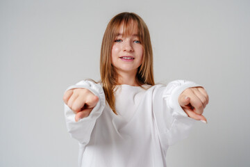 A young girl in a white sweatshirt playfully poses with finger guns against a neutral background