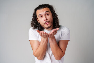 A man with curly hair blows a kiss to the camera while wearing a white t-shirt