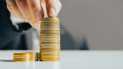 hand placing a coin on a stack gold coins