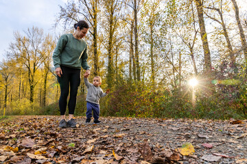 Fototapeta premium Mother and Toddler Walking in Autumn Forest Pathway