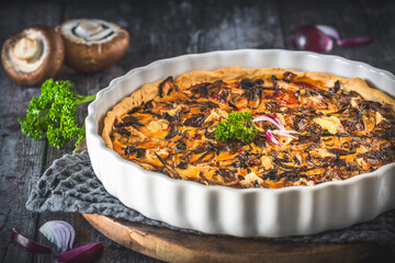Tart, quiche, with caramelized mushrooms, red onions and parsley on a dark background