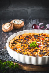 Whole tart, quiche with caramelized mushrooms, red onions and parsley on a dark background, vertical