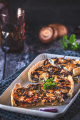 Tart, quiche with caramelized mushrooms, red onions and parsley on a dark background, vertical