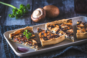 Tart, quiche, with caramelized mushrooms, red onions and parsley on a dark background