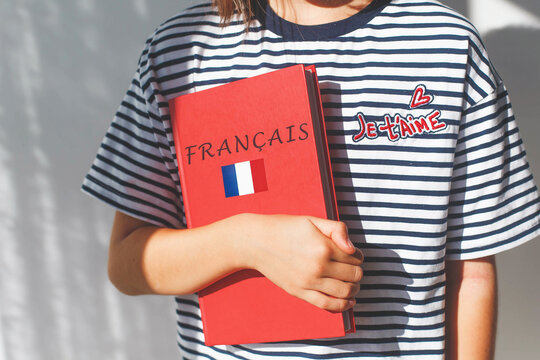 one white girl child schoolgirl with t-shirt with i love you in french and french textbook with french inscription and flag of France, foreign language learning concept