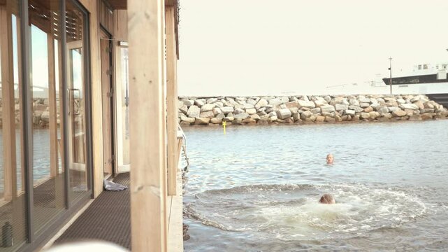 4K footage of Jumping woman into cold Fjord water from Scandinavian floating sauna deck. She shining with happiness and relaxation perfectly capturing serene and invigorating sauna experience