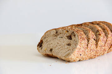 Slices of healthy whole grain raisin and walnut brown bread on the right against white background, with bread crumbs, healthy eating and lifestyle, balanced diet concept